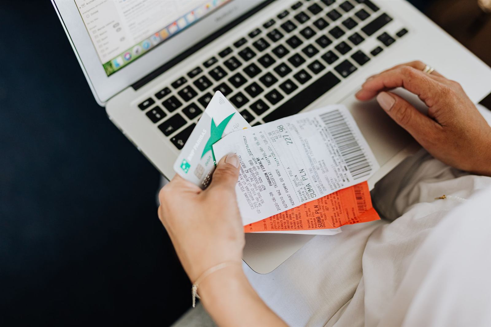Hands holding receipts and a bank card in front of a laptop
