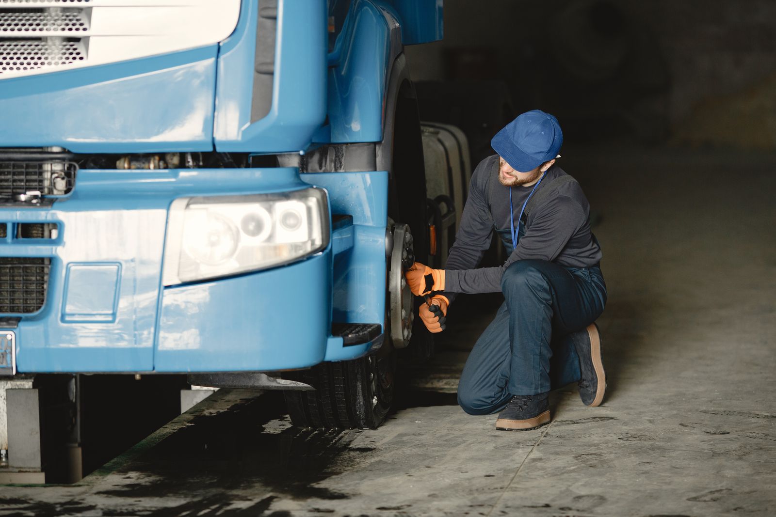 Mechanic kneeling to check the front wheel of a blue lorry in a workshop